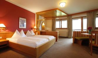 A cozy hotel room with a double bed and wooden details. Bright windows provide plenty of natural light and an inviting atmosphere.