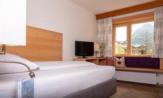 A modern hotel room with a large bed and a cozy atmosphere.  
Large windows offer a view of the mountains and plenty of daylight.