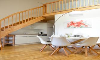 A bright, modern apartment with an open kitchen and a dining area. A wooden staircase leads to the upper floor.