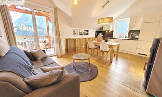 Modern apartment with a cozy living room and open kitchen. Large windows offer a beautiful view of the mountain landscape.