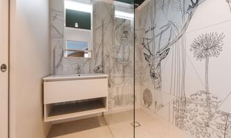 A modern bathroom with a glass shower cabin and a minimalist sink design. The walls are adorned with a creative, graphic design.