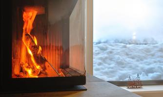 A cozy fireplace with flickering flames. Outside, a snow-covered landscape is visible.