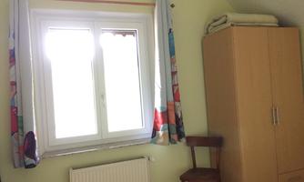 A simple room with a window that lets in daylight. Next to the window stands a wardrobe and a chair.