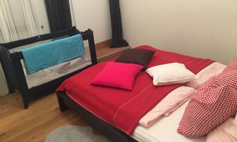 A cozy bedroom with a large bed and colorful pillows. Next to the bed is a children's bed with blankets.
