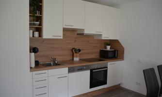 A modern kitchen with white cabinets and wood paneling. It is equipped with a stove, a microwave, and kitchen utensils.