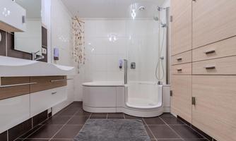 A modern bathroom with a shower and a bathtub. The walls are kept in light colors, and there are elegant wooden cabinets.