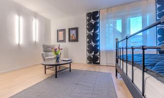 A modern bedroom with a bed and an armchair. Large windows provide plenty of daylight and a cozy atmosphere.