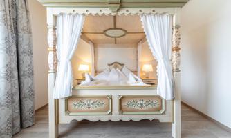 An elegant four-poster bed with white curtains and decorative details. The room feels bright and inviting.