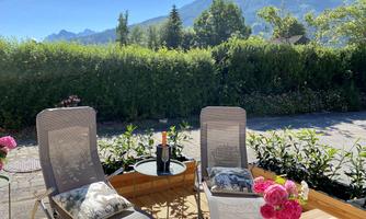 A sunny outdoor area with two loungers and a small table. In the background, green plants and mountains can be seen.