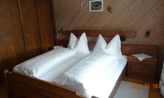 A cozy bedroom with a double bed and large pillows. The room has wooden walls and simple furniture.