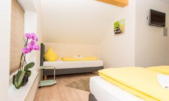 A cozy room with two beds and yellow bedspreads. An orchid and a small table complete the furnishings.