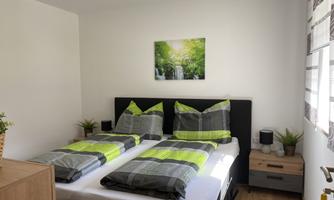 A modern bedroom with two single beds and green bedding. On the wall hangs a picture of a waterfall in a green landscape.