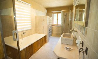 A modern bathroom with a bathtub and a large shower. The walls are light tiled, and a window provides natural light.