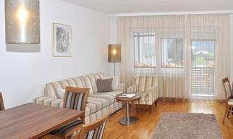 A modern living room with a comfortable sofa, a table, and a large window. The room is bright and inviting, with wooden flooring and elegant furniture.
