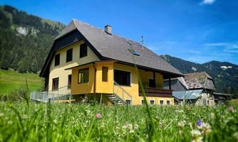 A modern house in bright yellow, surrounded by green meadows. In the background, gentle hills and forests are visible.