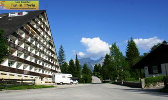 A modern hotel building in a picturesque setting. In the background, trees and mountains can be seen against a clear blue sky.