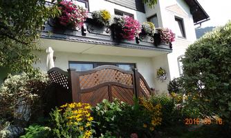 A charming house with blooming balcony boxes and a decorative wooden door. Surrounded by colorful flowers and lush greenery.