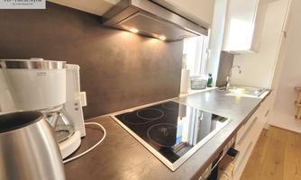 A modern kitchen with a dark countertop and light cabinets. The kitchen appliances, such as a coffee machine and a cooktop, are clearly visible.