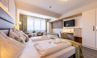 A modern hotel room with two beds, a television, and plenty of natural light. There is a cozy seating area and stylish decor.