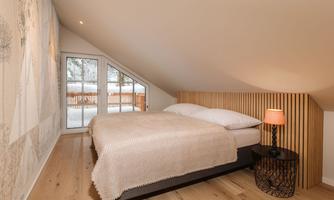A cozy bedroom with a double bed and a wood panel. Large windows offer a view of the outside environment.