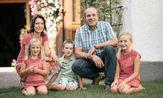 A family is sitting in the garden in front of a house. They are smiling warmly at the camera.