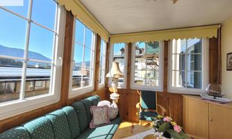 A cozy room with large windows and plenty of natural light. The furnishings include a green couch, a table, and a floor lamp.