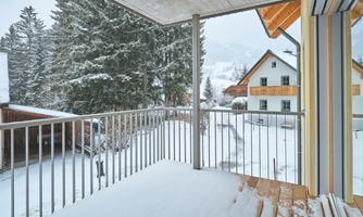 A snow-covered balcony overlooking snowy trees and buildings. The serene winter landscape conveys a peaceful atmosphere.