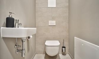 A modern bathroom with a wall-mounted toilet and a small sink. The walls are in subtle shades of gray.