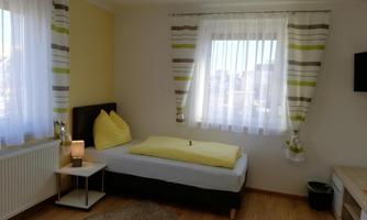 A cozy bedroom with a single bed and yellow pillows. The walls are painted light, and the window lets in plenty of daylight.