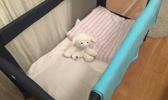 A cozy baby crib with a white pillow and a blanket. A stuffed animal lies in the middle of the crib.