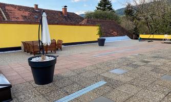 A rooftop terrace with a large yellow wall and cozy furniture. There are also some potted plants and sun umbrellas.