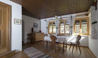 A cozy dining area with a wooden table and chairs. Large windows bring plenty of light into the room.