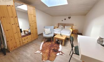 A cozy bedroom with wooden shelves and a large mirror. There is a bed, a desk, and a comfortable seating area.