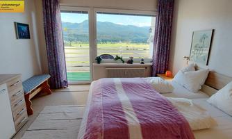 A bright bedroom with a large window that offers a view of the mountains and the meadow. The decor is modern and inviting, with a cozy bed.