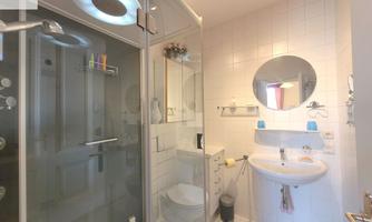 A modern bathroom with a shower, sink, and mirror. White tiles and a bright, functional design create an inviting atmosphere.