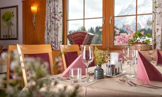 <p>A cozy set table in a restaurant with a view of the local mountain Grimming. The windows let in a lot of light and the decoration is inviting.</p>