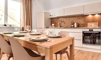 A modern kitchen with a wooden dining table. The table is set and the atmosphere is friendly and inviting.