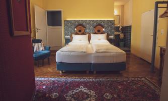 A cozy bedroom with a double bed and a colorful rug. The walls are painted in a warm yellow tone and there is a blue armchair in the room.