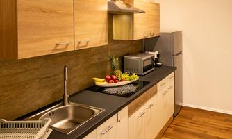 A modern kitchen with wooden cabinets and a dark countertop. Fresh fruits are standing in a bowl on the countertop.
