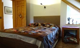 A cozy bedroom with a large bed and colorful sheets. Next to the bed is a small table and a window with a beautiful view.