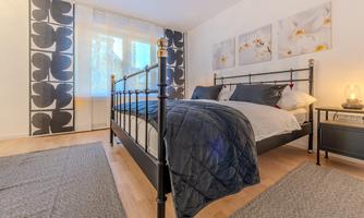 A modern bedroom with a black metal bed and cozy bedding. The walls are decorated with decorative pictures and an elegant curtain.