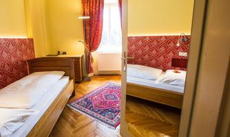 A cozy bedroom with two single beds and a colorful rug. The walls are designed in bright yellow and red, and the window lets in a lot of daylight.