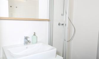 A modern bathroom with a white sink and a shower. The walls are bright and there are some decorative elements made of wood.