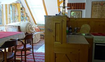 A cozy apartment with wooden details and large windows. The room features a seating area and a small kitchen.