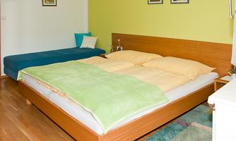 A bright bedroom with a double bed and a single bed. The walls are painted green, and small pictures hang on the wall.