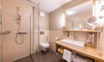 A modern bathroom with a shower and a sink on a wooden shelf. The walls are light and the lighting is friendly.