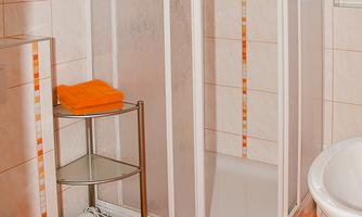 A modern bathroom with a shower cabin and a bathtub. The walls are light-tiled, and a stool with orange towels is ready.