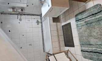 A modern bathroom with a bathtub and a sink. The walls are tiled, and there is a wooden towel rack.