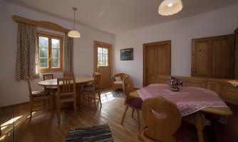 A bright dining room with wooden flooring and natural light. There is a round table with chairs and a cozy atmosphere.