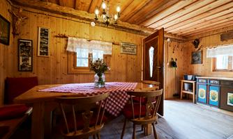 A cozy room with wooden walls and a large table. On the table is a vase of flowers, and there are chairs as well as a pretty kitchen cabinet.